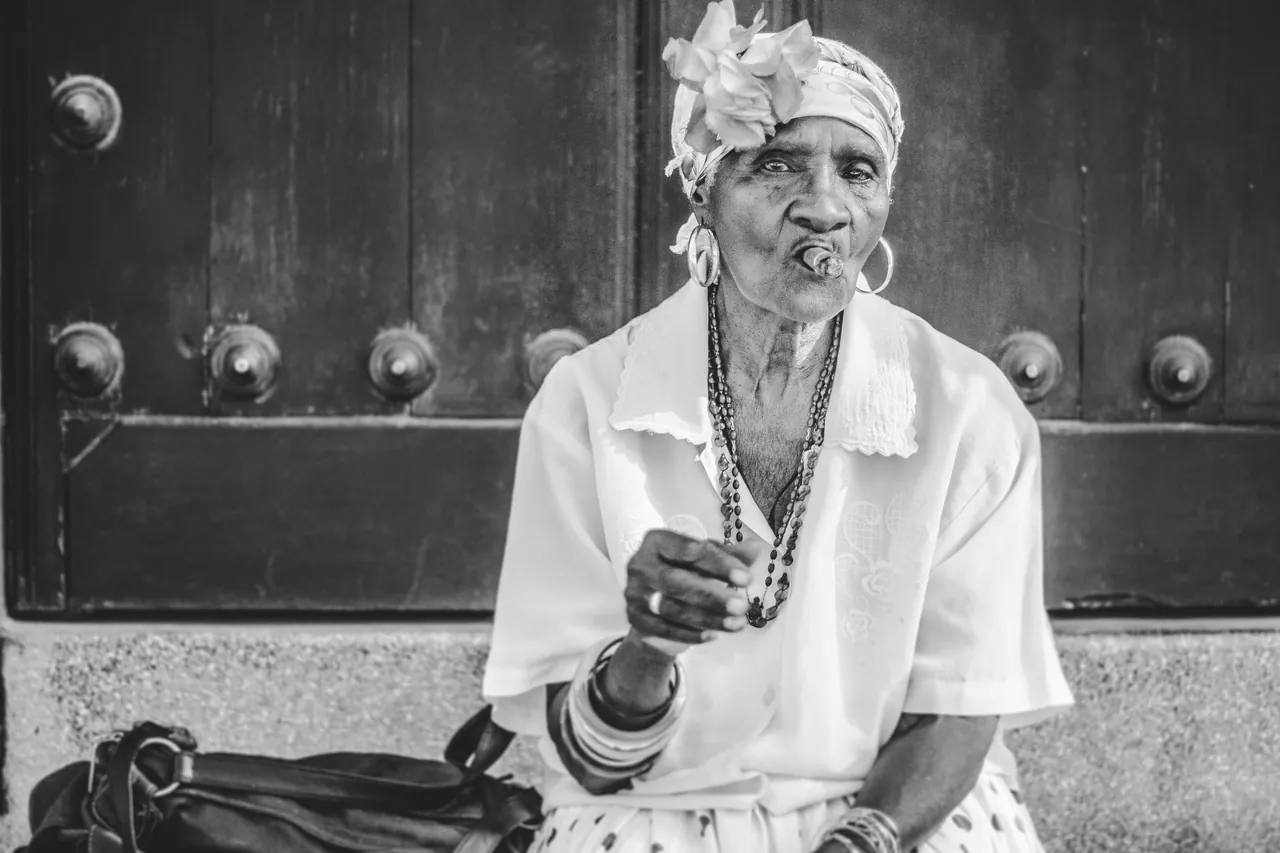 Old black woman smoking a cigar while sitting in front of an old building. Photo by Ellen Carlson.